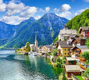 Hallstatt, Austria. View to Hallstattersee Lake and Alps mountains summits. Ancient houses at lake banks with chapel. Summer day. Blue sky with clouds.